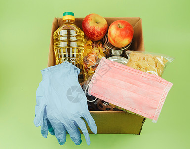 纸板箱 为有需要的人捐赠绿色背景的食物 送餐和病毒防护 医用手套和面罩 捐赠和怜悯的概念背景图片