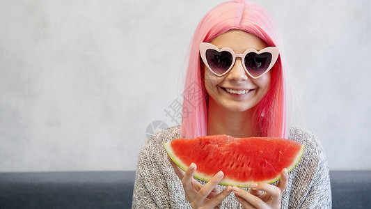 女人戴着粉红色假发和心形眼镜 穿着粉色假发太阳水果海滩食物乐趣牛仔裤西瓜饮食配饰产品背景图片