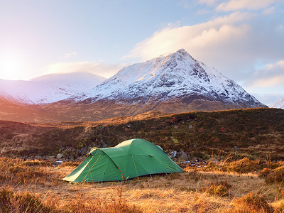 1021米高的斯托布·迪尔格山雪锥体下河流草原上草地上的绿色旅游帐篷背景