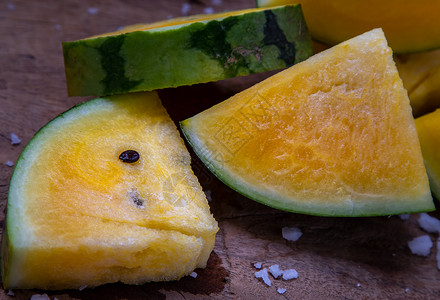 黄色的西瓜新鲜多汁的黄色西瓜在旧木背景上切成三角形热带营养椭圆形甜点水果静物异国农业种子情调背景