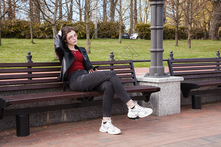 女孩坐在城市公园的长椅上露面眼镜城市黑发成人电话街道公园晴天绿色女性背景图片
