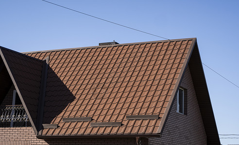 屋面素材安装在现代房屋上的棕色波纹金属型材屋顶 波纹板屋顶 金属型材波浪形屋顶 现代屋顶由金属制成 金属屋面房子窗户山墙聚合物建造建筑建背景