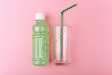 透明瓶子 有浅绿色脱毒饮料 与空玻璃旁边的清绿酒杯和明亮粉红背景的绿稻草背景图片
