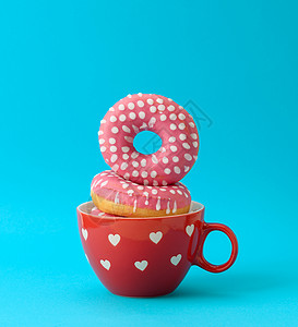 粉色甜甜圈一堆粉红色甜甜圈 蓝色背景的红陶瓷杯里有结冰背景