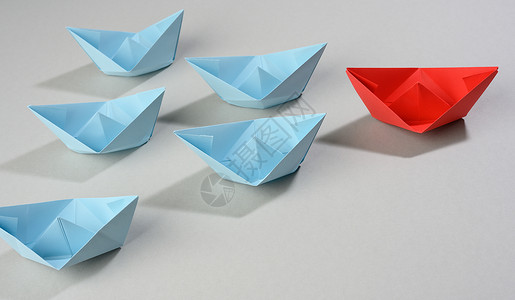 灰色背景的纸船小组 一个团队中强力领导的概念 操纵群众 一折纸经理团体老板血管折叠竞赛蓝色玩具舰队背景