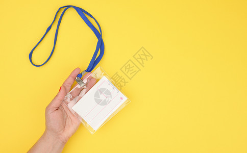 女性手拿着黄色背景上蓝色挂绳上的透明塑料徽章背景图片