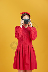 在黄色背景上拿着照相机的年轻美女 惊艳游客成人女孩相机旅行女士女性摄影乐趣技术背景图片