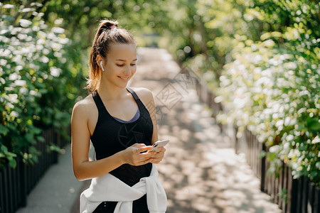 手机列表素材运动作为生活方式 专注于智能手机的健康苗条运动女性的水平镜头检查信息 并从穿着运动服的播放列表中选择歌曲 在户外呼吸新鲜空气背景