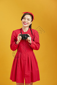 在黄色背景上拿着照相机的年轻美女 惊艳摄影女士摄影师照片乐趣技术女性相机女孩旅行背景图片