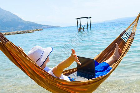 年轻微笑的女人 穿草帽的女自由职业者 在海滩上用笔记本电脑工作自由职业女人享受开发商学习科技海洋天堂世界远程背景图片