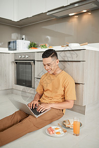 帅哥坐在地板上 拿着笔记本电脑和早餐一起跪着背景图片