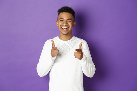 欢乐的非洲美国年轻人的画面 指着镜头 微笑 赞美良好的选择 祝贺某事 站立在紫色背景上 掌声学生工作爆炸促销工作室广告运动衫潮人背景图片