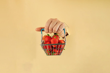 装着草莓篮子女孩手里拿着一个购物篮 里面装着成熟的红草莓 女人的手在撕破的纸上 网上购物的概念美食购物饮食农业水果销售大车零售购物车甜点背景