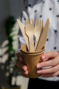 叉子o型女性手握着木质叉子和带有板块的纸杯 生态友好型可支配餐具 用于快餐 餐馆 外卖 野餐生活方式健康生活用具家庭工艺回收生物浪费纸板背景