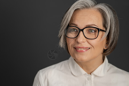 白衬衫的漂亮白发女人 聪明的中年女商务人士戴着眼镜 中等长度的护理发型在灰色背景下微笑 特写肖像 左侧的文本空间背景