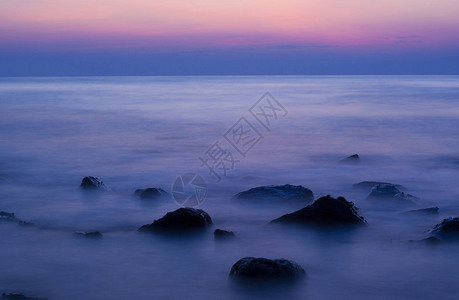 晚上在岩石海滩上柔软的波浪日落海洋橙子蓝色地平线天空风景低速海岸孤独背景图片