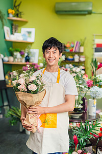 英俊的男花匠站在花店里 拿着一束花朵花束店铺植物销售快乐园艺花艺零售男性商业背景图片