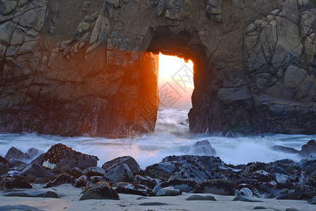 穿透洞的光线海岸日落岩石海浪海滩阳光海景悬崖背景图片