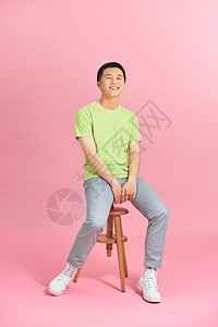 穿着T恤的人坐在一张椅子上 在粉红色墙壁前的男人的长相男性冒充凳子微笑工作室商业影楼背景图片