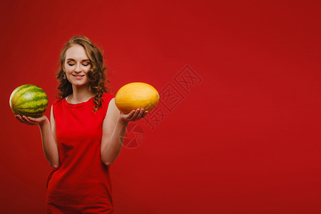 西瓜中的女孩照片中 一个身穿红色裙子的可爱女孩微笑着 手里拿着西瓜和甜瓜 在鲜红色背景中突显背景