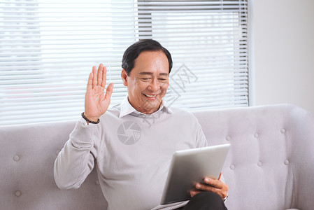 亚裔高官手持平板电脑做视频电话技术沙发爸爸退休父亲男人呼唤伙伴药片互联网背景图片
