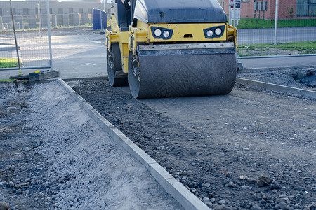 在道路工程和新的人行道建设期间 在新铺设的柏油布上安装工作卡车工业机器运输挖掘机黄色拖拉机车辆滚筒背景图片