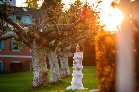 穿着白婚礼服的新娘 位于奥地利城镇的一个公园中 日落时有大树长发婚礼女士裙子压痛形象建筑学村庄青年魅力背景图片