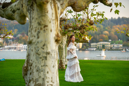 穿着白婚礼服的新娘 位于奥地利城镇的一个公园中 日落时有大树形象裙子婚礼魅力空气长发女士长裙树木建筑学背景图片