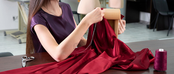 在裁缝工作室或餐饮店缝制红裙子的 美丽的年轻女服装匠织物职场工作女裁缝女性女士作坊成人女孩剪裁背景图片