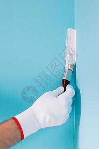 持有油漆笔刷和画蓝墙的男子工具男人设备修理手套工艺蓝色建造业家装成人背景图片