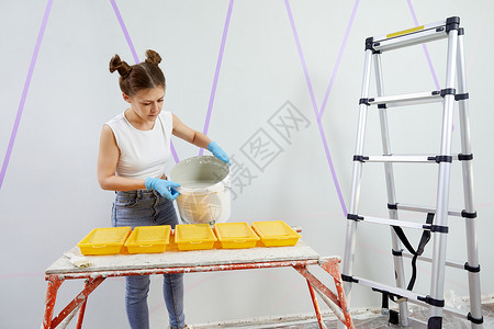 青年妇女将涂料倒入塑料油漆托盘梯子房子白色女性维修公寓装修工具滚筒家居背景图片
