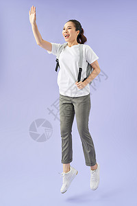 年轻快乐的女士 背背包跳跃和庆祝成功 孤立在紫色背景年轻的高清图片素材