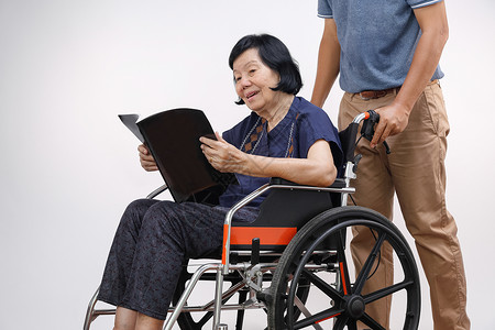 与儿子一起看轮椅的书的老年妇女要小心男人杂志照顾者祖母女士母亲退休男性家庭幸福背景图片