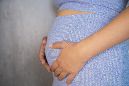 一名孕妇穿着蓝色西装 手放在灰色背景上 抱着她的腹部和双手母性婴儿会议宝宝家庭母亲宫缩奇迹妈妈产妇背景图片