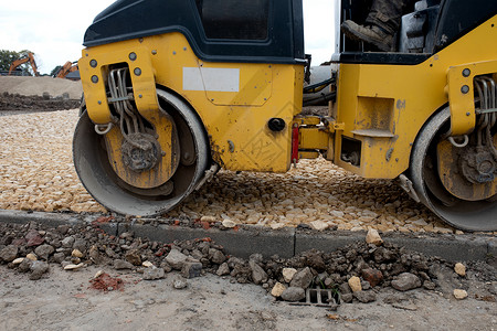 在道路工程和新的人行道建设期间 在新铺设的柏油布上安装工作车辆车轮挖掘机卡车运输拖拉机机器机械建筑背景图片