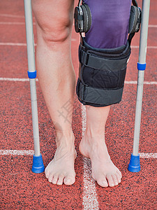 康复辅具患有用棍棒走路和膝盖支架支持外科手术的妇女背景