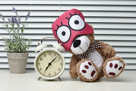 棕色泰迪熊坐在白桌上睡觉时带绷带 在闹钟附近 早上7点到图片