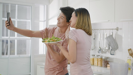 使用智能手机现场直播和沙拉食品的男女两性博主烹饪技术微笑沙拉女性夫妻幸福女士自拍背景图片