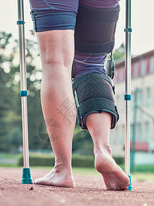 康复辅具妇女在被医疗棍棒打伤后用膝盖围着膝部走路拐杖骨科支撑灵活性运动膝关节手腕骨头矫形器赤脚背景