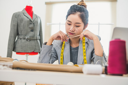 职场达人毛笔字在家庭办公室车间工作的迷人亚洲女性时装设计师 时尚的时尚达人女性创造新的布料设计系列 裁缝和缝纫 人们的生活方式和职业概念工艺衣背景