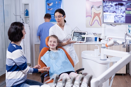 牙齿缺失的小女孩在牙科检查穿着围嘴时对父母微笑背景图片