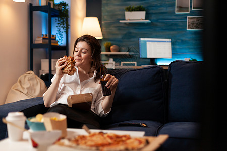 开心女人吃美味美食 美味的送货汉堡 在沙发上放松看喜剧电影背景图片