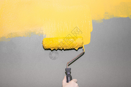 一位画家将明亮的黄色油漆滚到灰色的墙壁背景上 房间画 潘通色背景图片