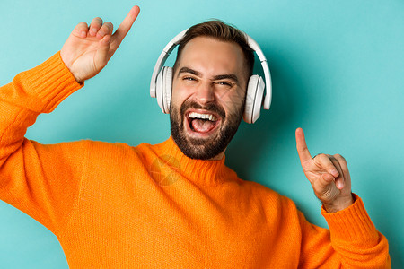 耳机促销x展架穿着橙色的毛衣 站在绿宝石背景上 坐在绿色的羊皮衫上 以耳机收听音乐潮人胡子购物男人横幅手势橙子快乐男性标识背景