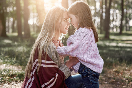 一个女孩在森林里亲吻母亲女士微笑婴儿孩子树叶快乐母性家庭女儿公园背景图片