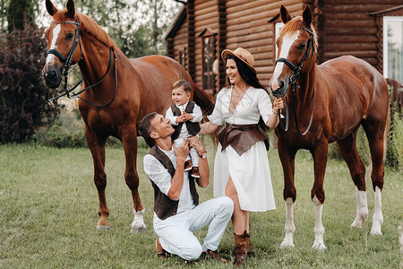炫父日白衣家庭与儿子一起站在两匹美丽的自然马旁 一对有孩子的时装夫妇被用马拍下照片 a 一名男子牧场女士白色马术童年爸爸日落妈妈牛仔父背景