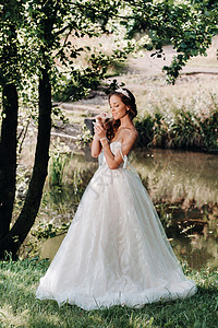 一位穿着白色裙子的优雅新娘 在公园的瀑布上戴着花束的手套 享受着大自然 穿着婚纱和手套的模特在森林里 白俄罗斯旅行婚姻石头黑发女背景图片