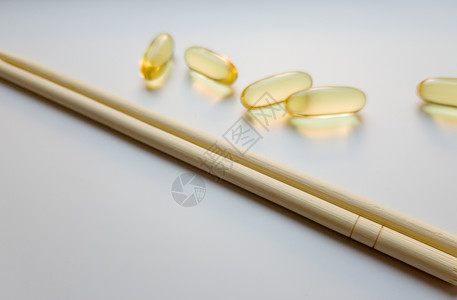 鱼油胶囊用中国筷子 在白色背景上的欧米茄 3 高分辨率产品 食物供给 健康生活方式的维生素 脂肪酸 体内新陈代谢处方愈合药品胶囊背景图片