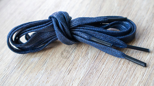一张深蓝色的平板鞋带片子 上面有鞋子的细小提示 卷起来 在木制背景上被隔离花边单品蓝色纺织品蕾丝物品配饰绳索线圈自色背景图片