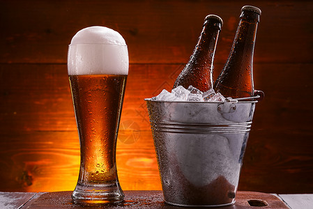 啤酒冰两瓶啤酒放在一桶水里 加冰和一杯啤酒 在黑暗背景旁用红泡沫黄色干杯绿色玻璃饮料庆典生活瓶子酒精白色背景